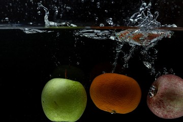 Fototapeta na wymiar Close up view of colorful fruits falling in water on black background. Gorgeous backgrounds.