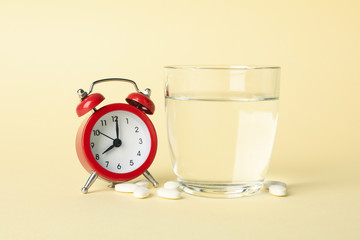 Alarm clock, pills and glass of water on beige background, close up