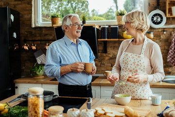 Happy mature couple talking while preparing food in the kitchen.