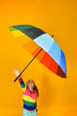 A girl in a colored sweater holds a multi-colored umbrella in her hand on a yellow background, a child and the colors of the rainbow.