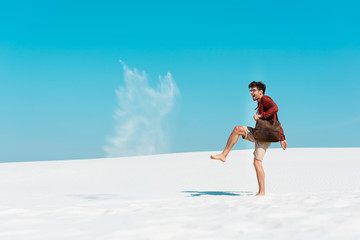 happy man with leather bag throwing sand in air on beach