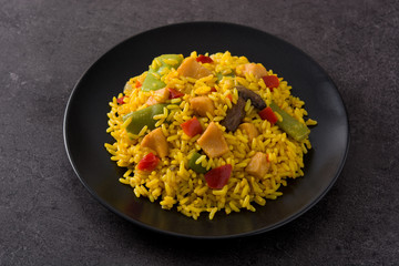Fried rice with chicken and vegetables on black plate on black background