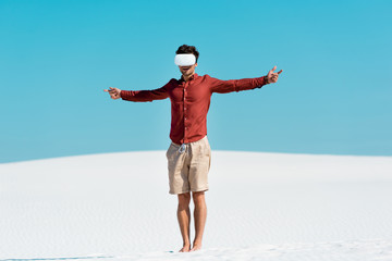 man on sandy beach in vr headset with open arms against clear blue sky