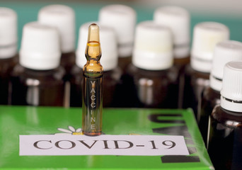 Ampoule inscription with vaccine on a green box, with the inscription COVID – 19. There is much small glass bottles beside.