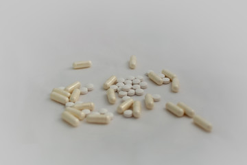 Bunch of pills - tablets and capsules - on white background. Selective focus. Light yellow capsules and white tablets are scattered over a white background. Virus cure.