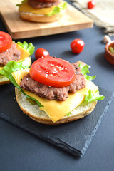 homemade cheeseburger on a wooden board with cherry tomatoes and pickles on a black background