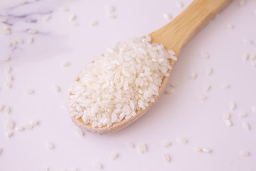  rice wooden spoon on white marble background. close-up, sprinkled rice