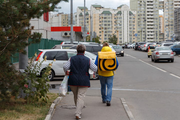 Woman with purchases and a man from a delivery service with a backpack walk down the street in the city.