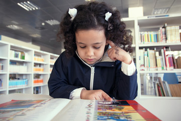 Niña leyendo un libro en la mesa de lectura.
