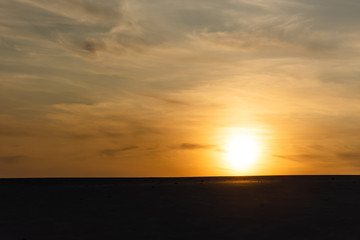 Fototapeta na wymiar dark sandy beach against bright sun during sunset