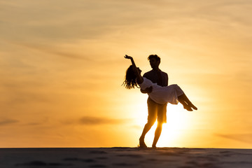 Fototapeta na wymiar silhouettes of man spinning around woman on beach against sun during sunset
