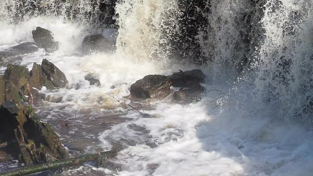close up shot of a rapid stream of water hitting a rock and creating a splash. Nature in Estonia. Very Strong raging river.