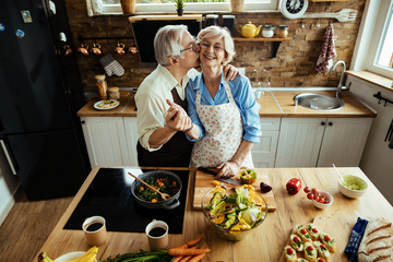 Happy mature couple showing affection while preparing healthy food in the kitchen.