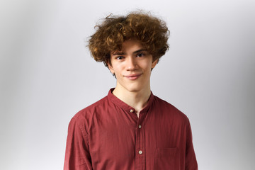 Fototapeta na wymiar Isolated shot of clean shaven cheerful young European guy with curly hair smiling at camera being in good mood, rejoicing at positive news. Joy, success, positiveness and happiness concept