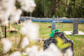 Naklejka premium Ancient grave with tombstone and cross on top. Spring day commemoration of the dead. Prayer for the souls of our relatives, friends, relatives and ancestors. A branch of blooming cherry.