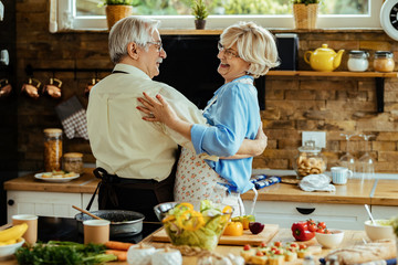 Happy senior couple talking while dancing in the kitchen.