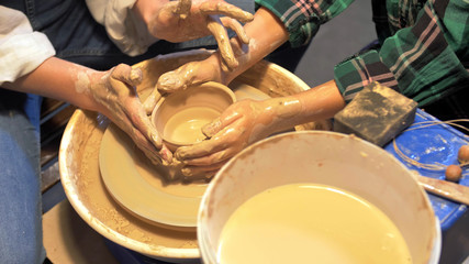 Fototapeta na wymiar Boy and woman works with pottery wheel in a workshop, slow motion