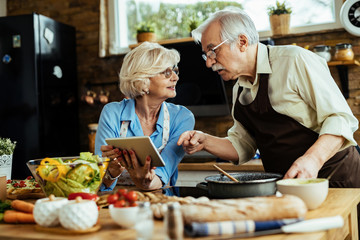 Mature couple using digital tablet while cooking together in the kitchen.