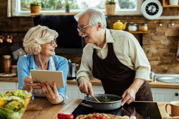 Happy senior couple talking while cooking and using touchpad in the kitchen.