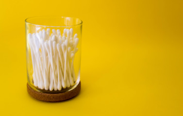 cotton swabs inside glass small container with wooden top. Yellow background. Free copy space....