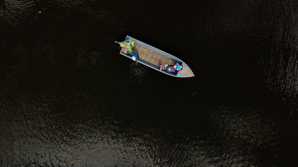 Aerial top view of a boat with three indigenous local people on dark green waters. A baby looking up, a man paddling. 