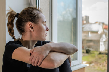 Obraz na płótnie Canvas Young girl sits on a windowsill near the window