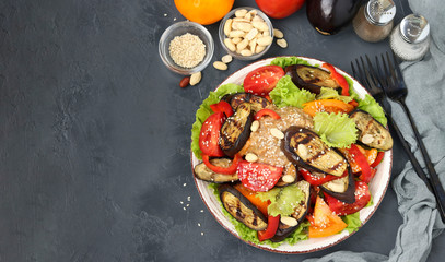 Salad with eggplant, tomato, paprika, lettuce, sesame, peanuts paste dressing, top view on dark background, copy space