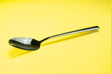 Löffel wirft Schatten einer Gabel auf einen gelbfarbenen Hintergrund