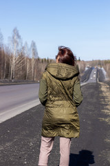 A young woman walks by the side of the road. Road in the forest