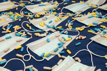 A many medical masks with colored pills on blue backdrop in blurred perspective close up, Coronavirus COVID-19 prevention, diagonal background texture design