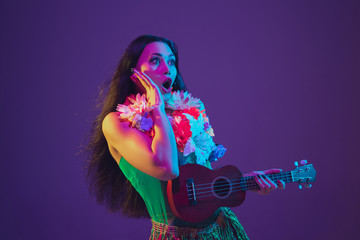 Fabulous Cinco de Mayo female dancer on purple studio background in neon light. Beautiful female model with ukulele, Mexico, Hawaii style. Celebration, holiday, music, beauty and fashion concept.