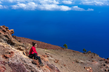 Fototapeta premium Young woman smiling with satisfaction, sitting on volcanic rock and relaxing after hike. Outdoor Lifestyle Photo. La Palma, Canary Islands, Spain.
