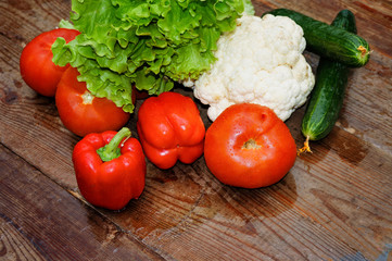 Fresh vegetables covered with drops of water bell pepper, cauliflower, lettuce, cucumbers, tomato on a background of an old wooden table close-up.