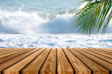 Fototapeta premium Brown wooden tabletop on blurred wave splashing in tropical sea with palm leaf