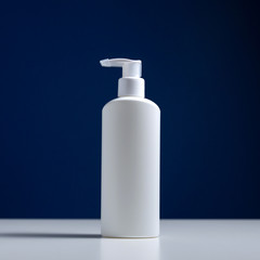 Plastic white antiseptic bottle with a dispenser on a blue background. The white package is on a white table.