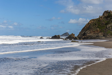 landscape of a dark sandy beach, rough sea blue sky, rocks in the sea