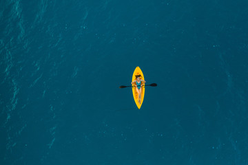 View from a drone of a girl sailing in a yellow kayak on a blue lagoon at dawn