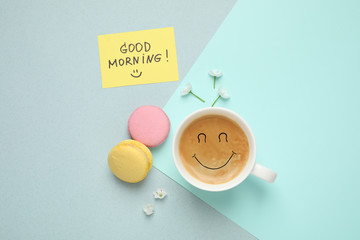 Delicious coffee, macarons, flowers and card with GOOD MORNING wish on color background, flat lay