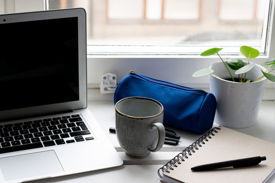 Working From Home Next To The Window With Laptop, Plants, Pen Case, Cup Of Coffee, Notebook And Pen On Table