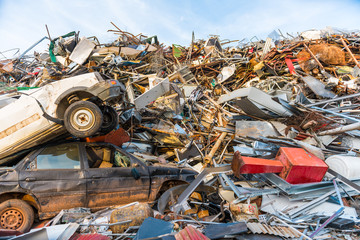Huge mountain of mainly metal garbage , appliances and a pair of cars in a junkyard.