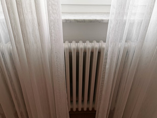 The central heating radiator is covered with light white curtains