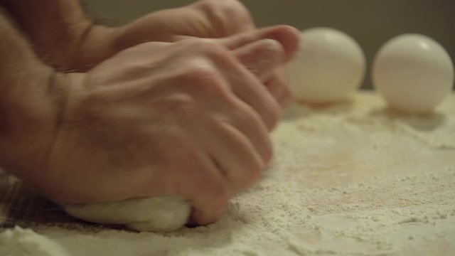 Man knead the dough dough on the kitchen table. Male hands knead the dough, close up. Man cooking food at home. Service to woman. Fresh flour is scattered around. Raw pizza dough. Real time 4k