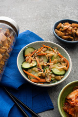 delicious kimchi in bowls and jar near chopsticks on blue cloth on concrete surface