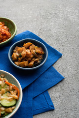bowls with tasty kimchi on blue cloth on concrete surface