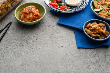 tasty kimchi in bowls and jar on blue cloth near chopsticks on concrete surface