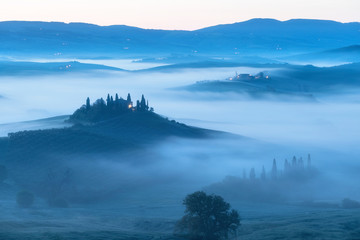 Beautiful colors of green spring panorama landscape of Tuscany. Most popular place in Italy. Green fields and blue sky and Cypress tree scenic road near Siena. Amazing foggy morning with sunshine
