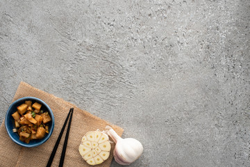 Obraz na płótnie Canvas top view of bowl with tasty kimchi, chopsticks and garlic on sackcloth on concrete surface