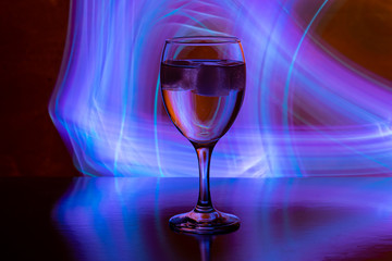 wine glass with ice on black background with neon light paintings behind.