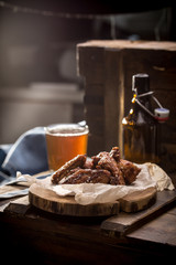 Chicken wings with sesame seeds and glass of beer with bottle on wooden background