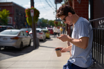 Enjoying city life. Handsome young man having coffee and typing sms. Province of Quebec, travel on Canada